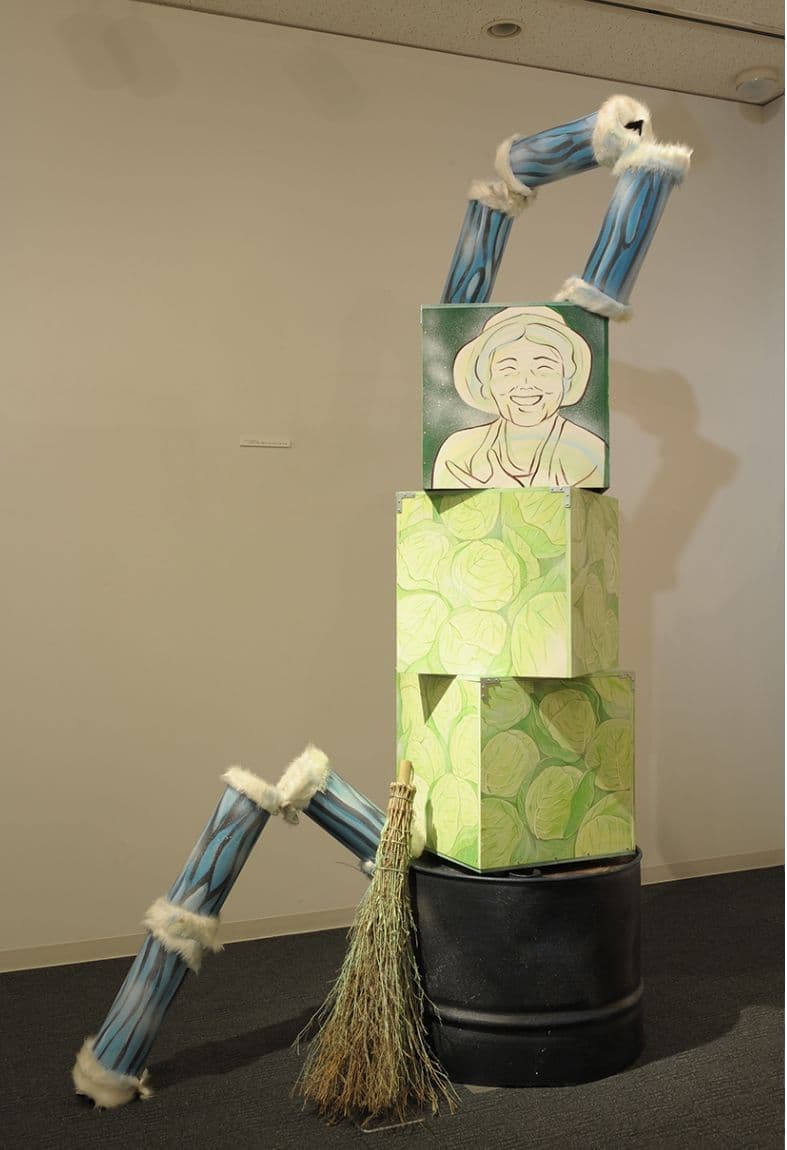 ドラムカンの上に絵が描かれた木箱が積み重なっているアート作品