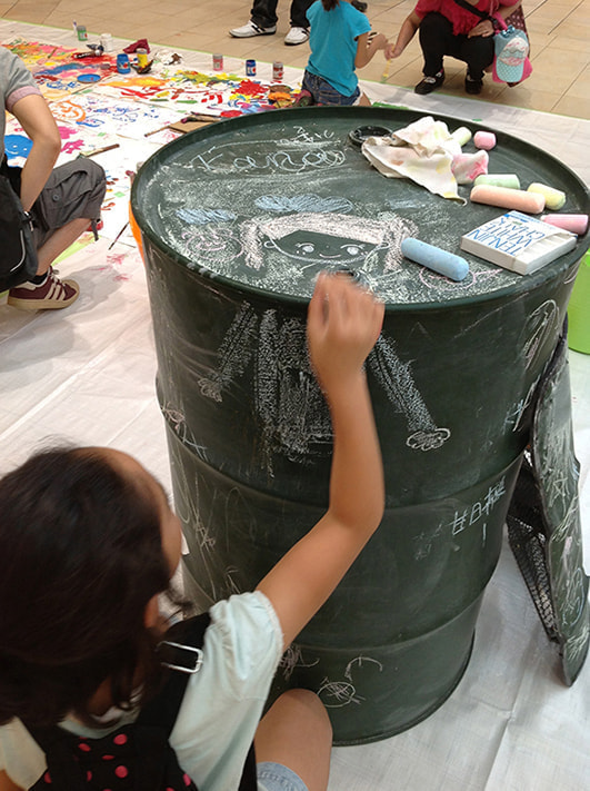 黒板塗装されたドラムカンに子供がお絵かき